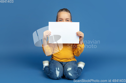 Image of Portrait of sad little girl sitting on blue studio background, autism concept