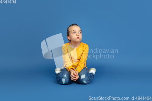 Image of Portrait of sad little girl sitting on blue studio background, autism concept