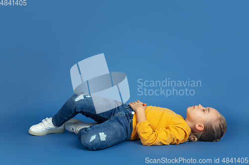 Image of Portrait of sad little girl sitting on blue studio background, autism concept