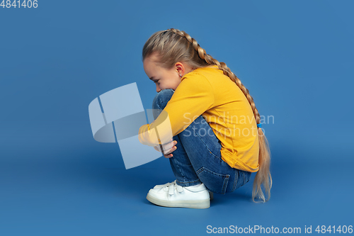 Image of Portrait of sad little girl sitting on blue studio background, autism concept