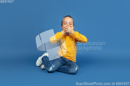 Image of Portrait of sad little girl sitting on blue studio background, autism concept