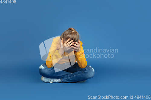 Image of Portrait of sad little girl sitting on blue studio background, autism concept