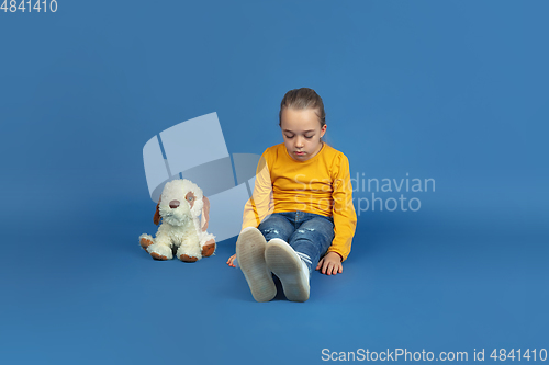 Image of Portrait of sad little girl sitting on blue studio background, autism concept