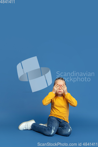 Image of Portrait of sad little girl sitting on blue studio background, autism concept