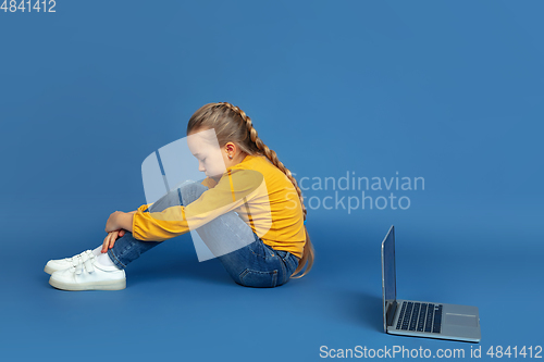 Image of Portrait of sad little girl sitting on blue studio background, autism concept