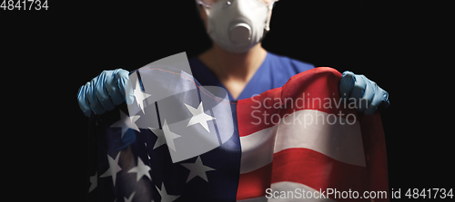 Image of doctor in goggles and mask holding flag of america