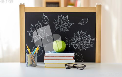 Image of books, apple and school supplies on table at home