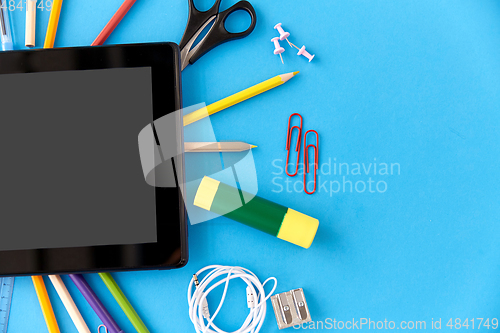 Image of tablet pc and school supplies on blue background