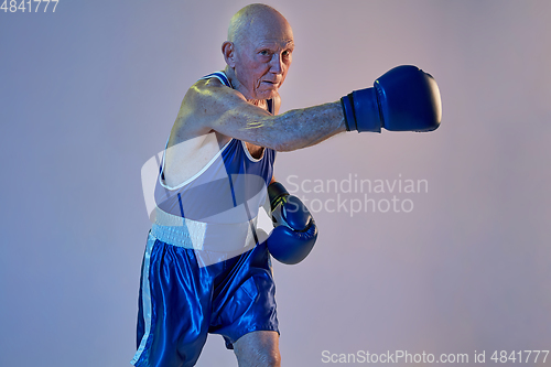 Image of Senior man wearing sportwear boxing isolated on gradient studio background in neon light. Concept of sport, activity, movement, wellbeing. Copyspace, ad.