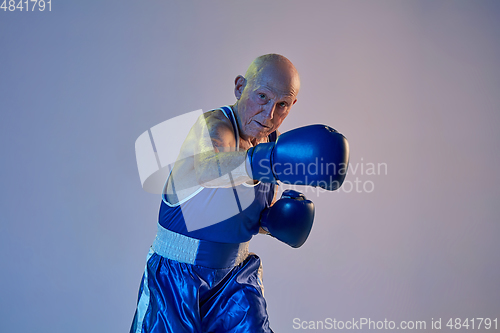 Image of Senior man wearing sportwear boxing isolated on gradient studio background in neon light. Concept of sport, activity, movement, wellbeing. Copyspace, ad.