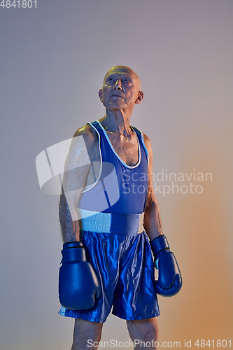 Image of Senior man wearing sportwear boxing isolated on gradient studio background in neon light. Concept of sport, activity, movement, wellbeing. Copyspace, ad.