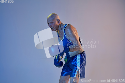 Image of Senior man wearing sportwear boxing isolated on gradient studio background in neon light. Concept of sport, activity, movement, wellbeing. Copyspace, ad.