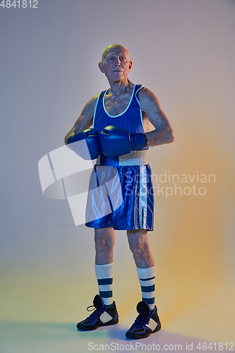 Image of Senior man wearing sportwear boxing isolated on gradient studio background in neon light. Concept of sport, activity, movement, wellbeing. Copyspace, ad.