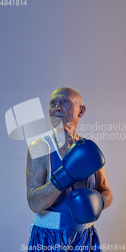 Image of Senior man wearing sportwear boxing isolated on gradient studio background in neon light. Concept of sport, activity, movement, wellbeing. Copyspace, ad.