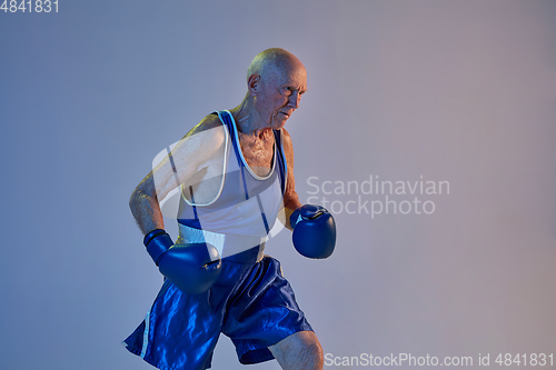 Image of Senior man wearing sportwear boxing isolated on gradient studio background in neon light. Concept of sport, activity, movement, wellbeing. Copyspace, ad.