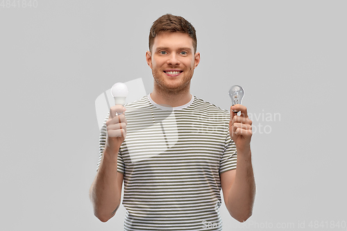 Image of smiling young man comparing different light bulbs