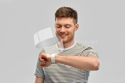 Image of smiling young man looking at smart watch