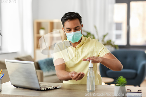 Image of man in mask using hand sanitizer at home office