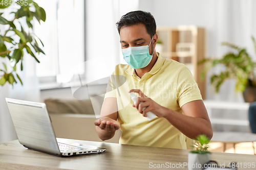 Image of man in mask using hand sanitizer at home office