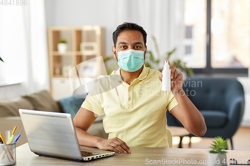 Image of man in mask with hand sanitizer at home office