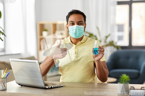 Image of man in mask with hand sanitizer at home office