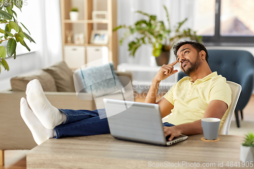 Image of man with laptop resting feet on table at home