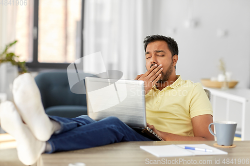 Image of tired man with laptop and feet on table at home