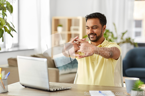 Image of happy man with laptop stretching at home office