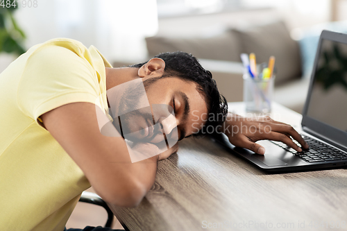 Image of indian man sleeping on table with laptop at home