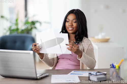 Image of happy woman with laptop and papers at home office
