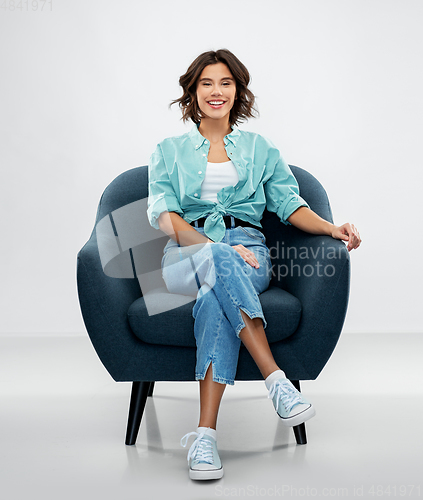 Image of happy smiling young woman sitting in armchair