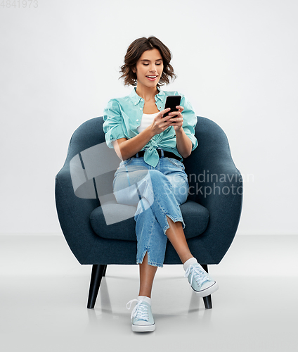 Image of happy woman with smartphone sitting in armchair