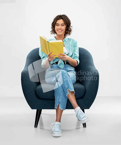 Image of happy young woman in armchair reading book