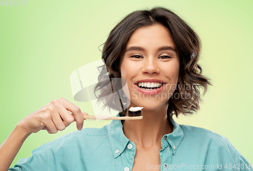 Image of smiling woman with toothpaste on wooden toothbrush