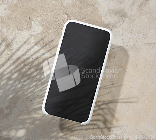 Image of smartphone on beige color table top with palm leaf shadow