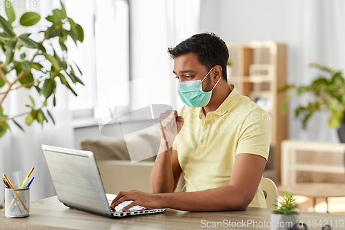 Image of sick indian man in mask with laptop works at home