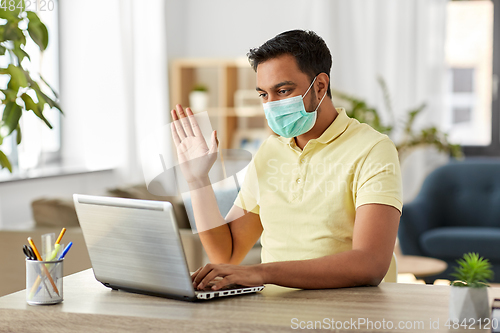 Image of man in mask with laptop having video call at home