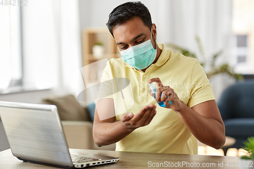 Image of man in mask using hand sanitizer at home office