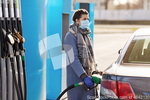 Image of woman in mask filling her car at gas station