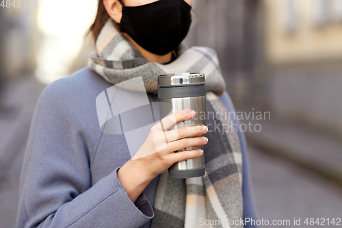 Image of woman in reusable mask with tumbler in city