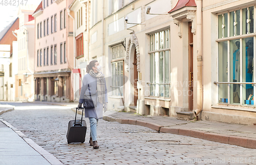 Image of woman in protective mask with travel bag in city