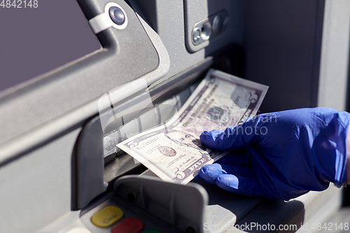 Image of hand in medical glove with money at atm machine