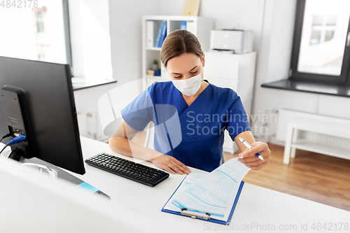 Image of doctor or nurse in mask with clipboard at hospital