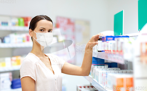 Image of female customer in mask choosing drugs at pharmacy