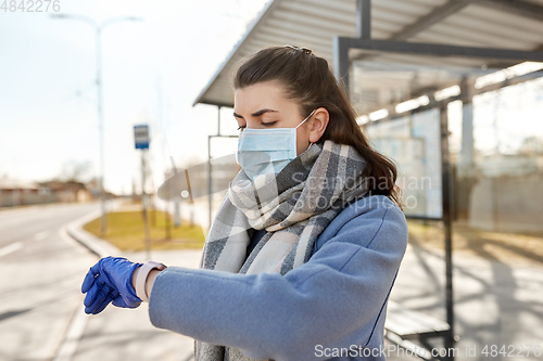 Image of woman in mask looking at wristwatch at bus stop