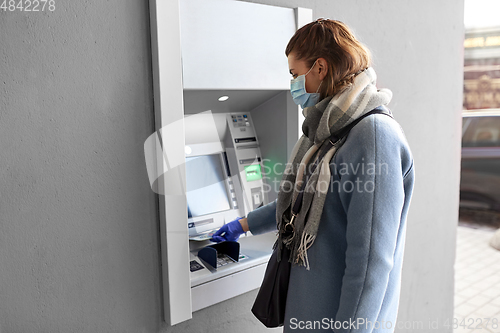 Image of hand in medical glove with money at atm machine