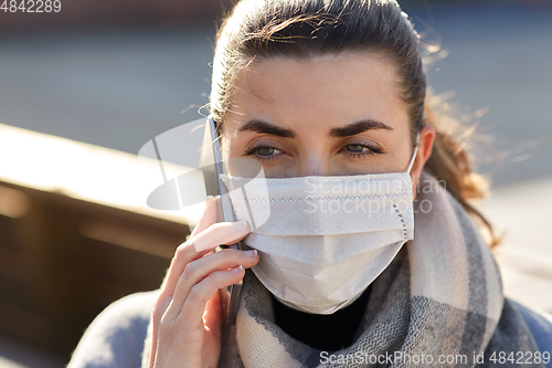 Image of woman in face mask calling on smartphone in city