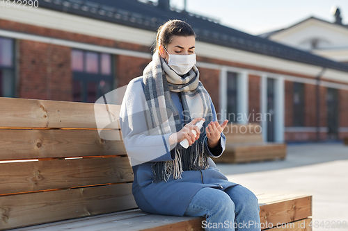 Image of woman in mask spraying hand sanitizer outdoors