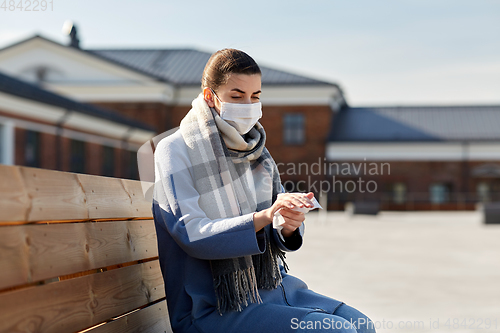 Image of woman in mask cleaning hands with antiseptic wipe