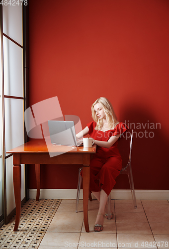 Image of Young adult woman sitting at the table and working on laptop